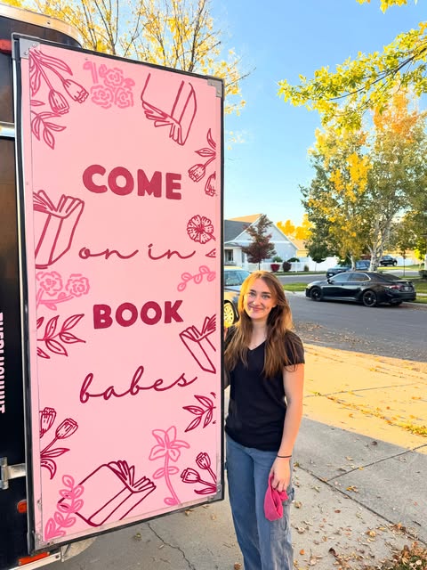 Ella beside a pink Come on in book babes sign on a trailer